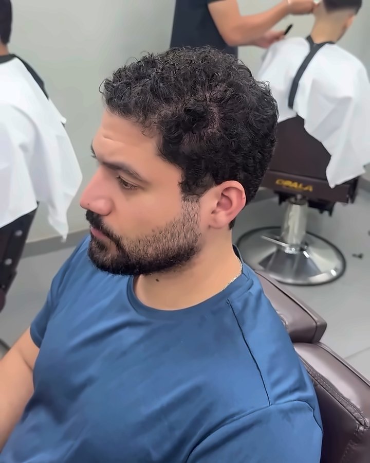 Cliente de barba e camiseta azul com o cabelo cacheado, antes