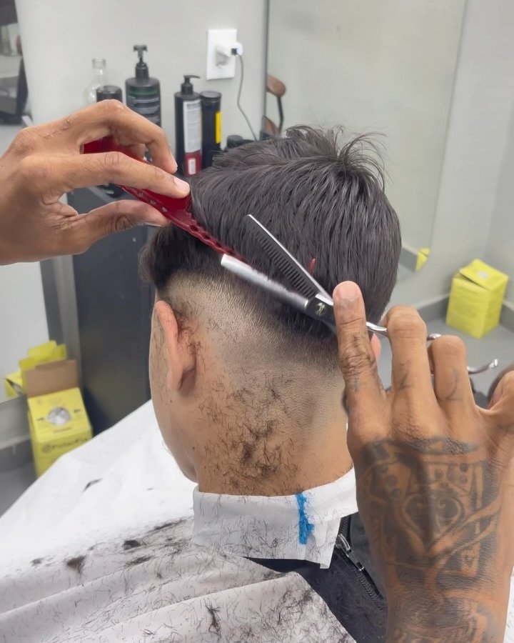 Barbeiro acertando o topo de um degradê com pente e tesoura